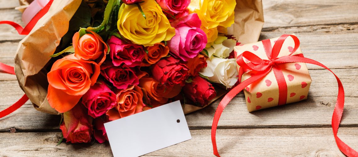 Bunch of roses and gift box with an empty tag on wooden background